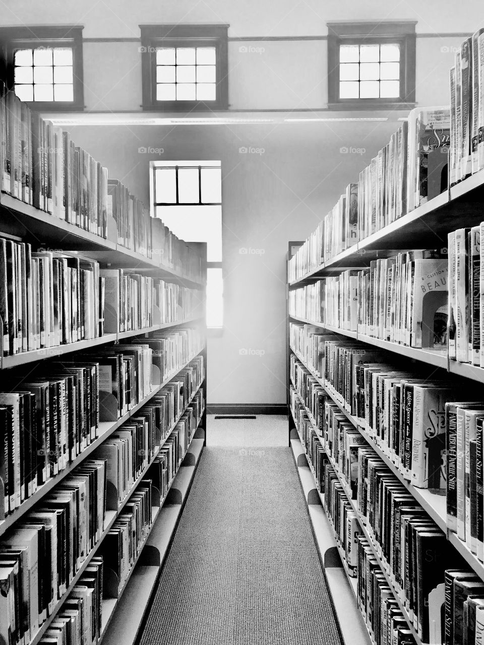 Interesting black and white photo of long row of bookshelves full of library books. 