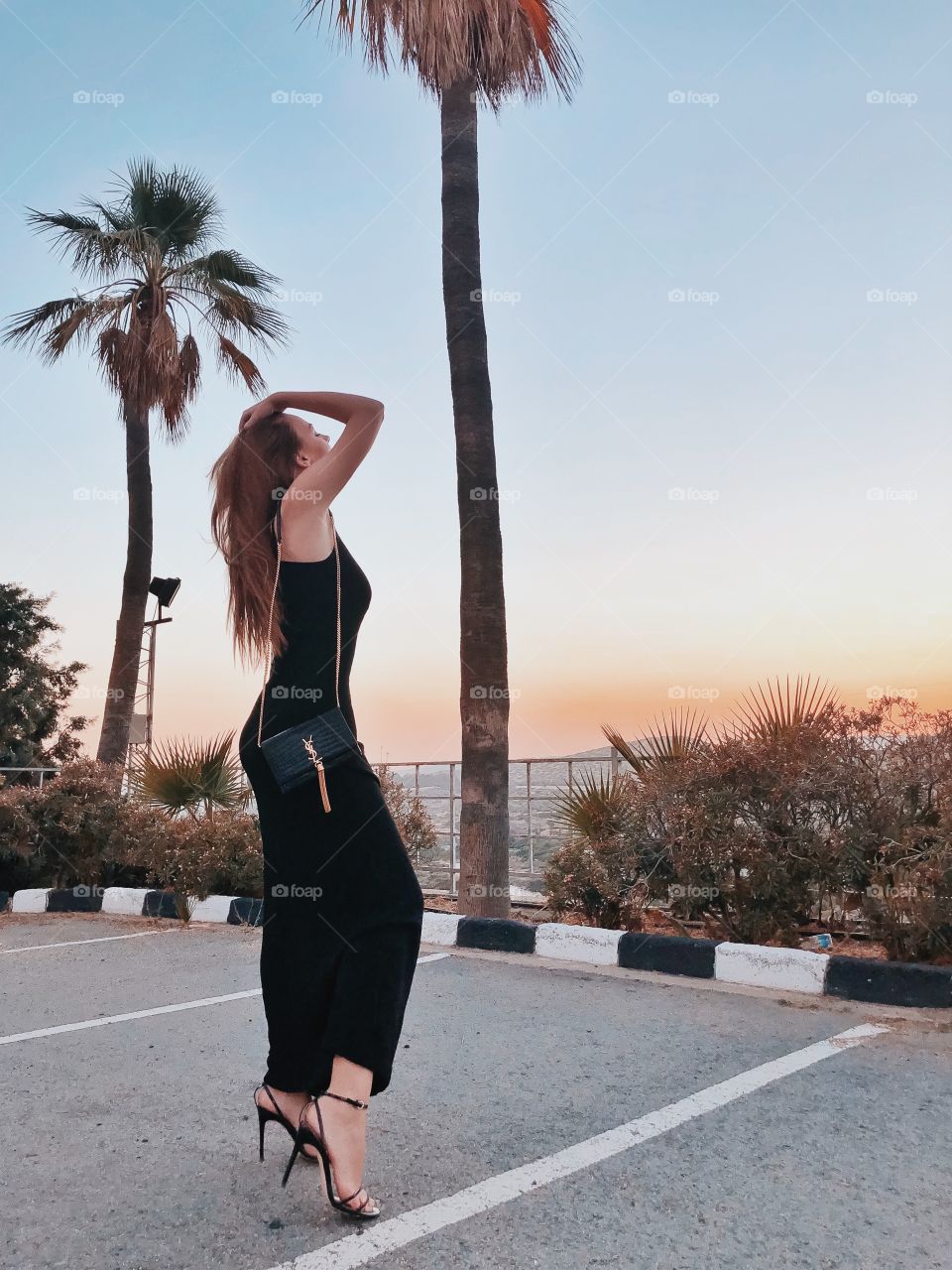 Beautiful elegant woman in black dress looking on sunset. Palms, beautiful nature. Luxury lifestyle. Street style. Fashion. Long hair. 