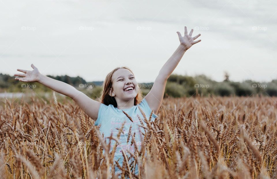 Happy beautiful tweens girl with long hair on the wheat field at sunset time