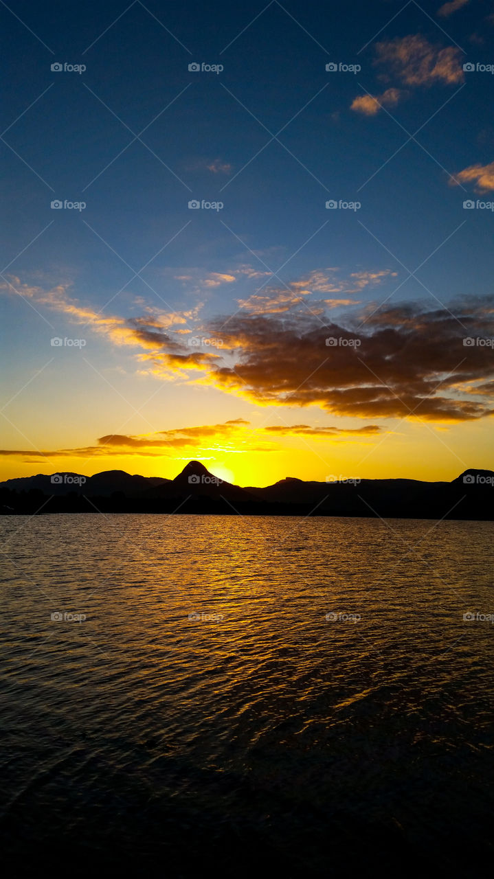 sunset over a lake with mountains and clouds in the air