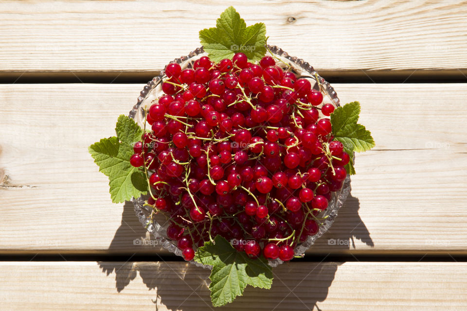 Red currant on glass dish placed on wood, from above 