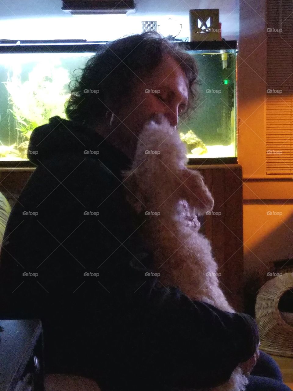 Dog being held lovingly by owner on her lap. She sits on couch with fishtank as background.