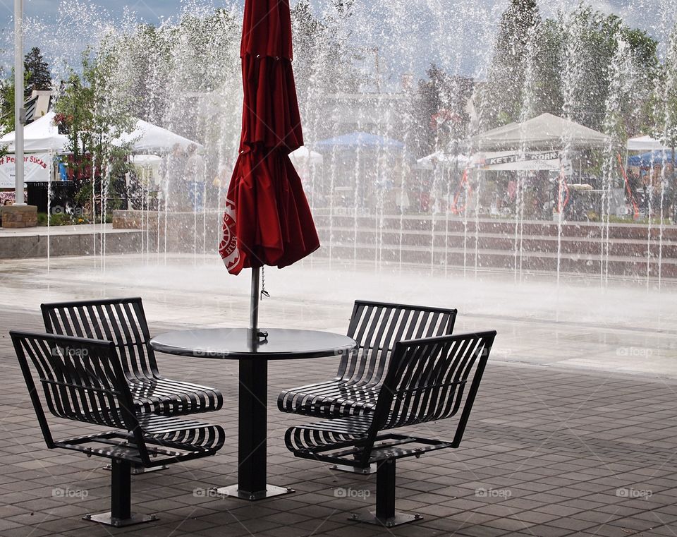 An outdoor table and chairs with a fountain in the background 