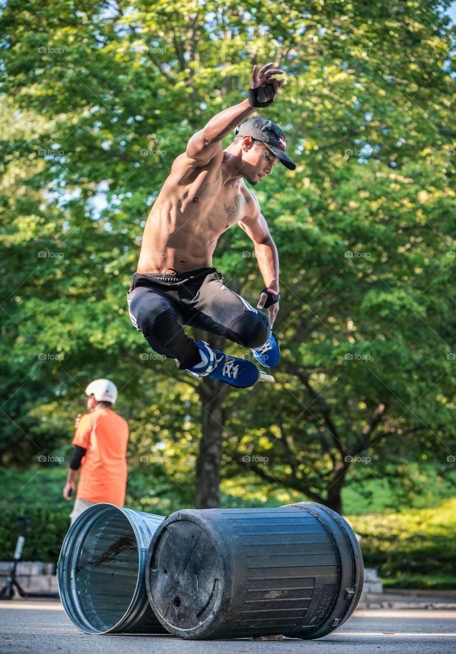 young man in roller skating jumps over trash cans in park.