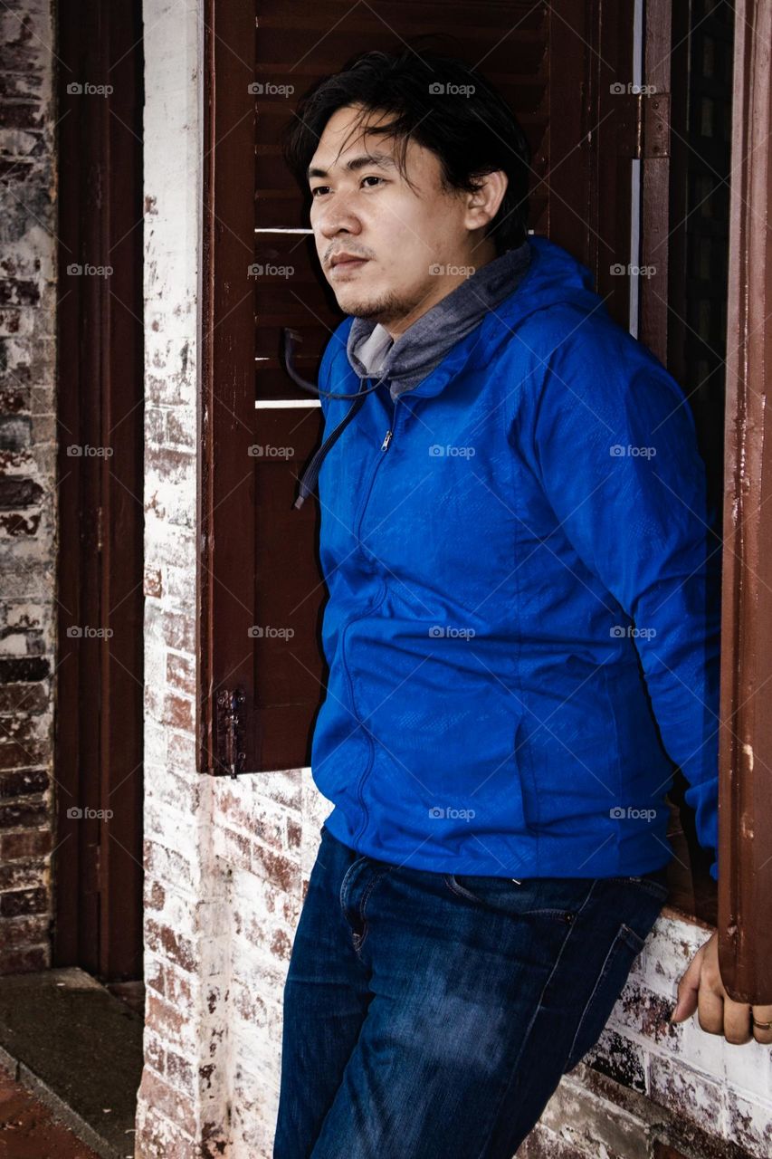 Asian men in blue standing outside the window of an old house looking away from the camera.
