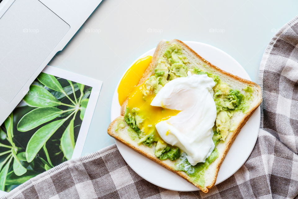 Sandwich with fresh green avocado, poached egg on white plate lying on gray background 