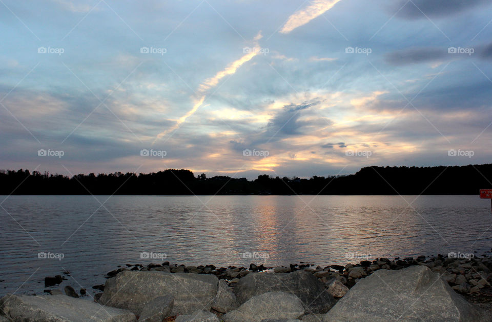 A beautiful creek with stones and rocks all around as the sun is quickly setting, and preparing for a new day, and the trees are swaying in the wind.