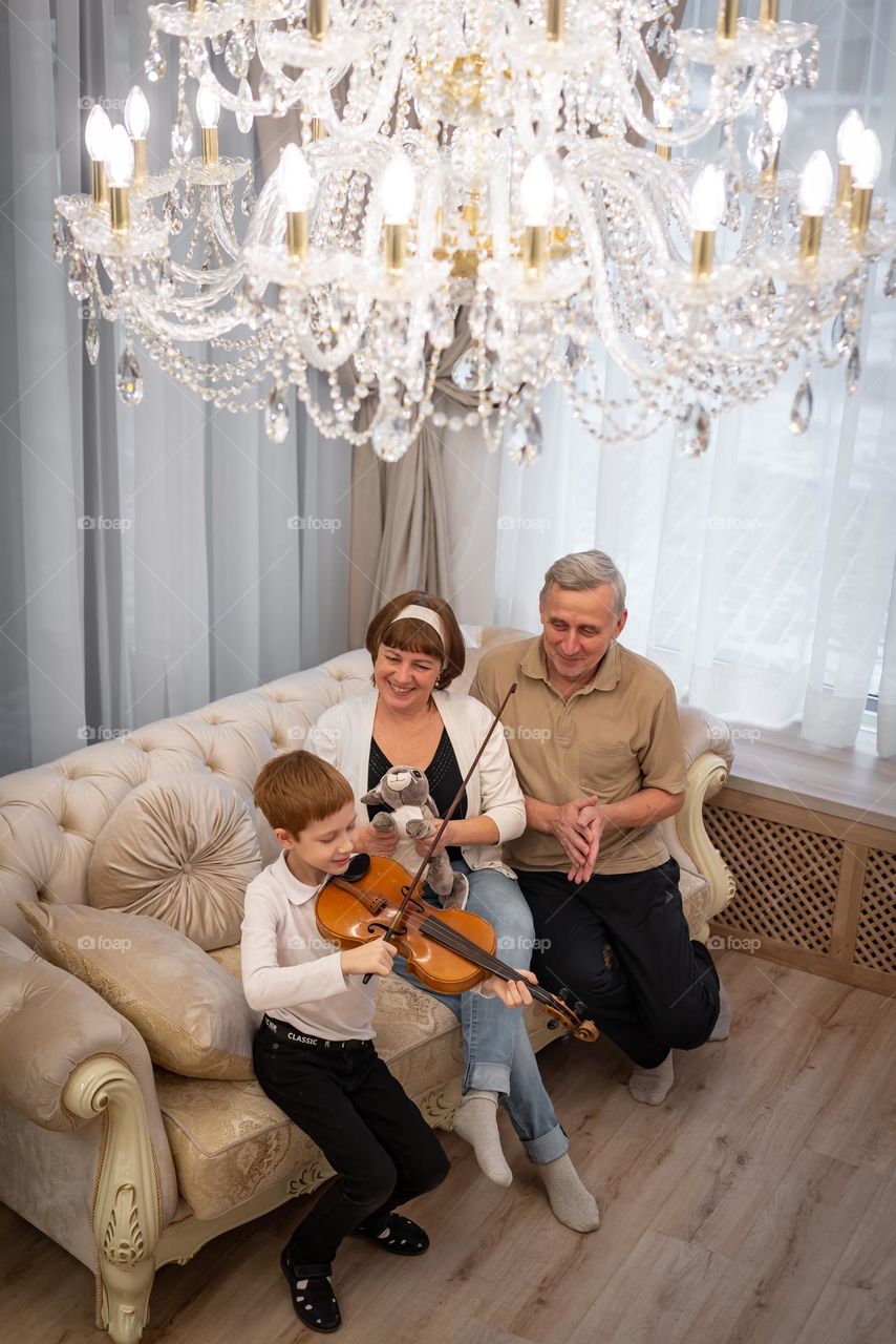 Red-haired boy plays the violin in a bright room, the family listens to music