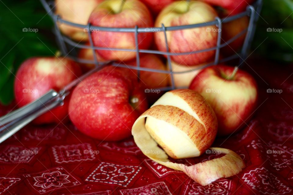 Fruits - Gala apples in a wire basket with a partially peeled apple and peeler on a red bandana-print tablecloth