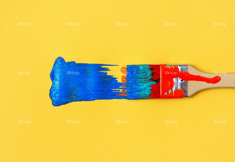 Colorful paintbrush with blue paint painting on yellow paper background