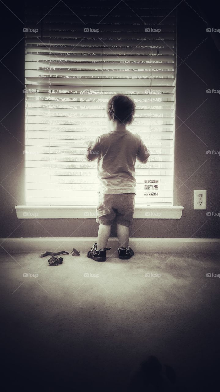 A little boy looking out the window waiting for mommy to come home.