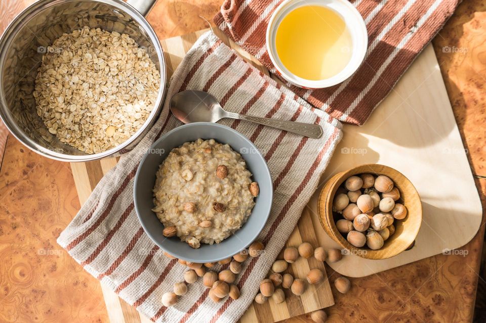 Cooked oatmeal in a deep gray plate with hazelnuts and honey.
