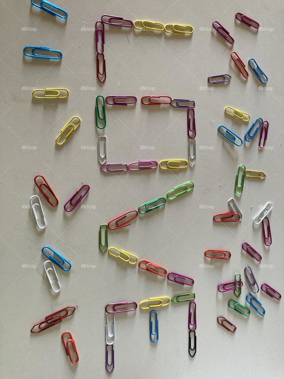 Mesa branca com palavra escrita com clipes coloridos, AMOR. Ao lado vários clipes espalhados para ornamentar a cena.