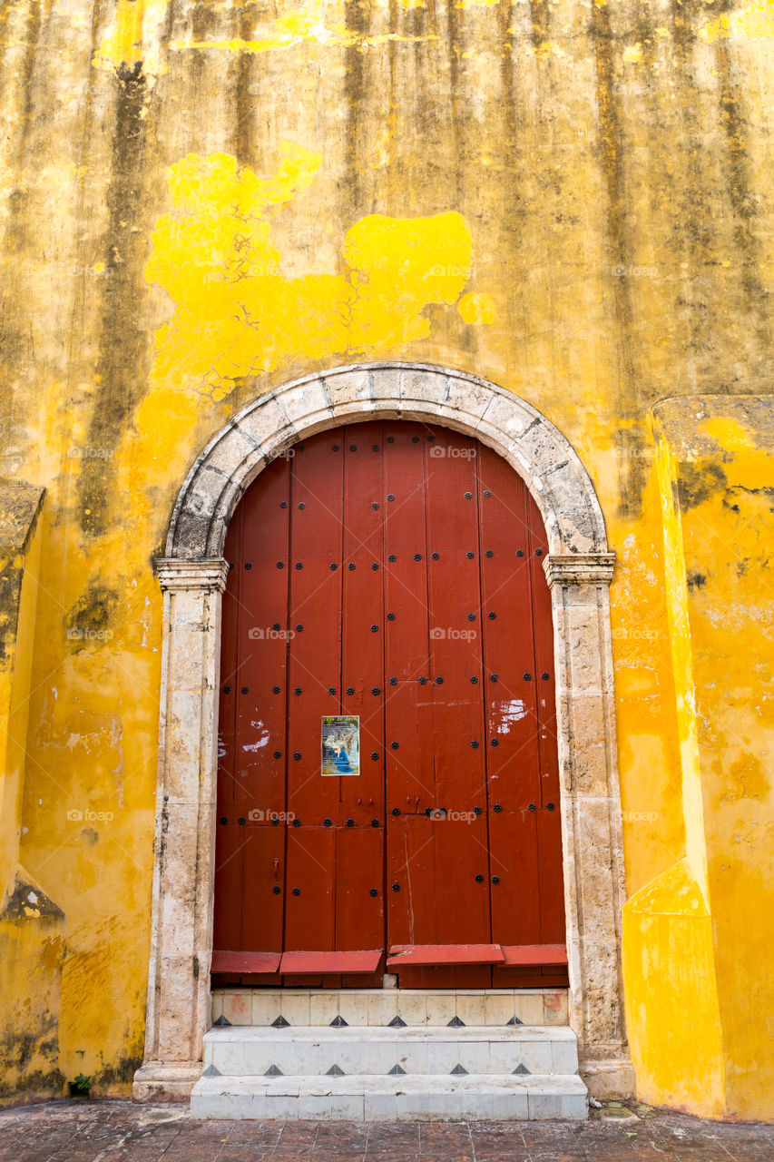 Red wooden door on a yellow building. Wooden brown double on a yellow building. Walls are dirty from pollution and aging. Paint had partially chipped off