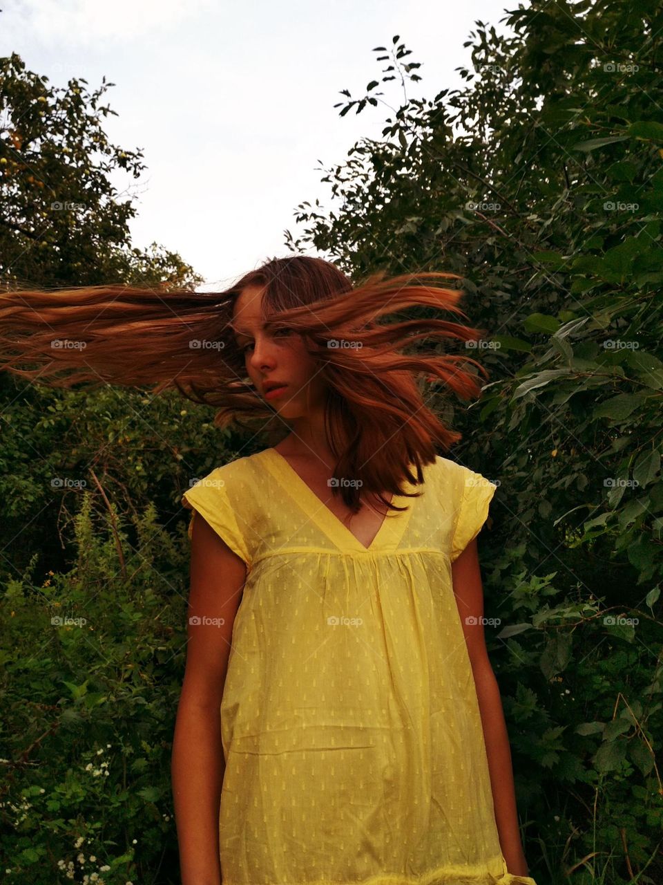 It is a photo of a young woman in the garden (apple trees). She has red (ginger) hair. She has brown eyes. She has medium lendth hair. She wears yellow dress