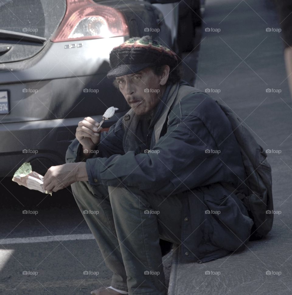 A poor man eating ice cream on road side in summer