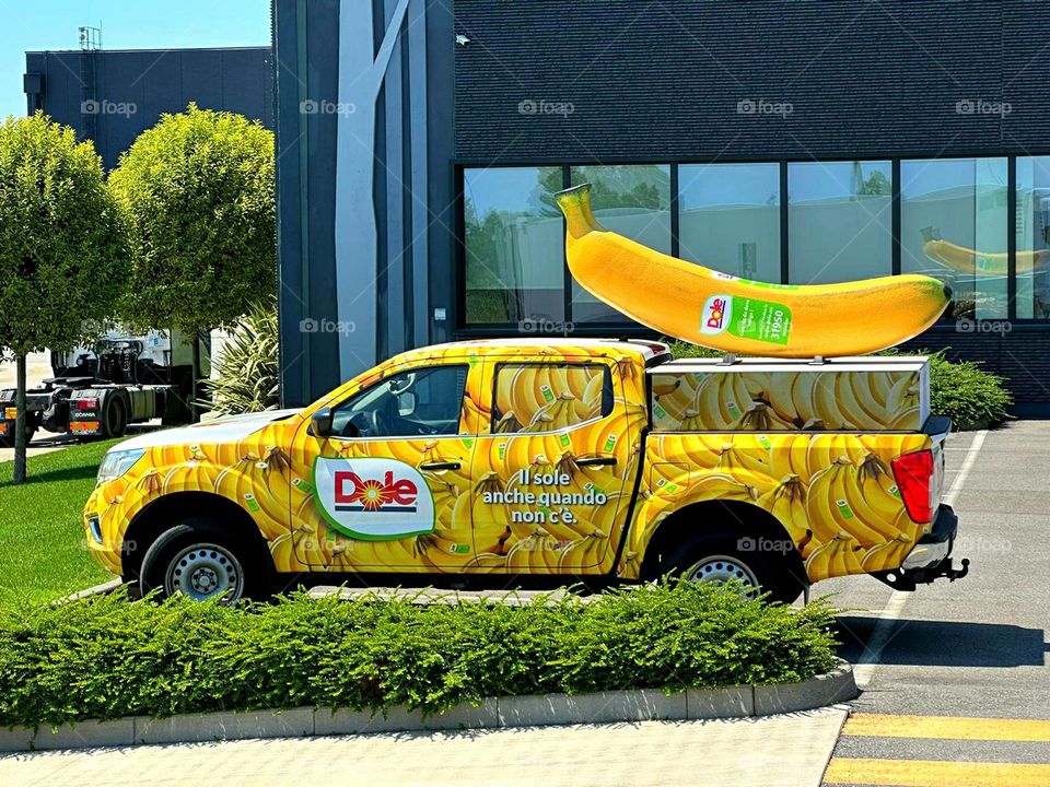 There is a yellow car near the grocery store, on the roof of which there is a mock-up of a banana. Italy