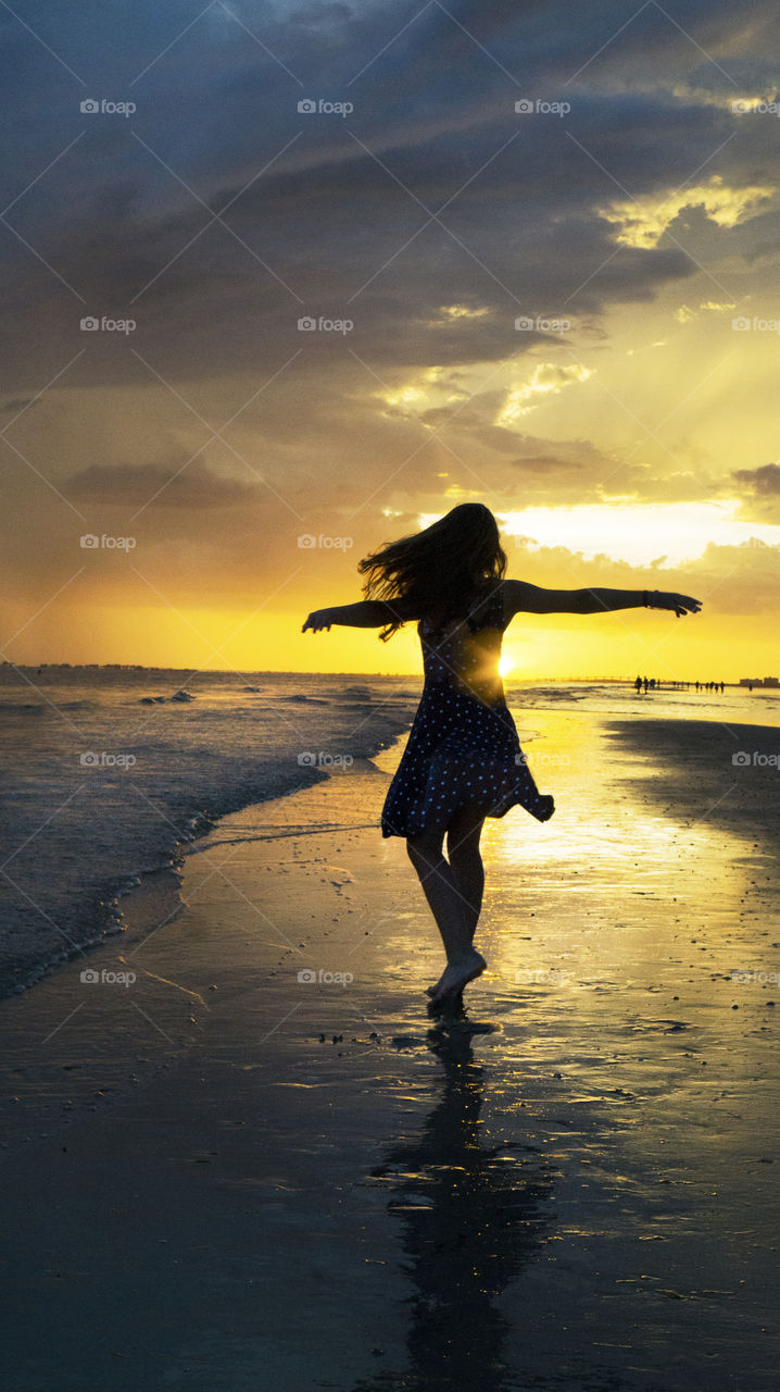 A young girl dances in the sunset as the sun rays bounce off her dress at the beach