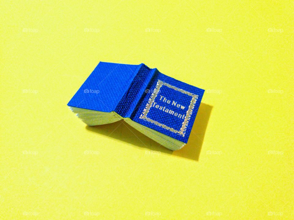 Minimalism - miniature royal blue Bible new testament on bright yellow background