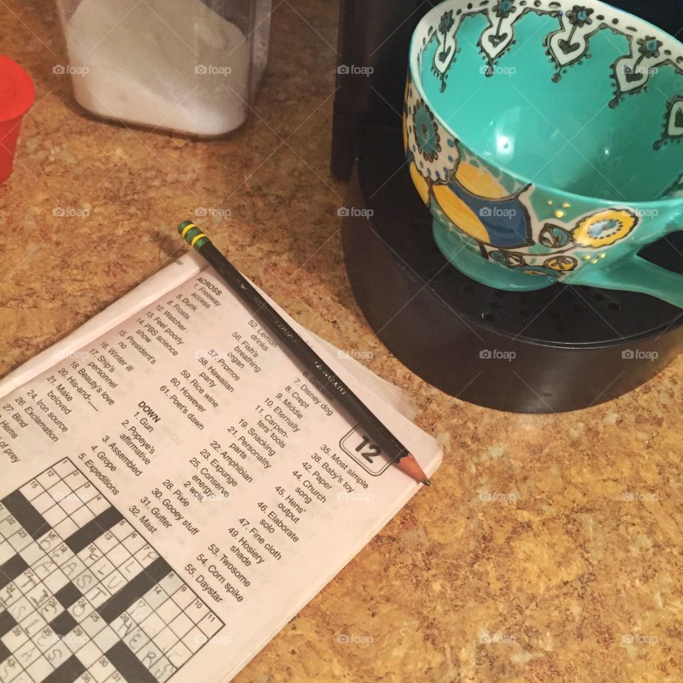 Coffee brewing. A crossword puzzle book next to a decorative mug