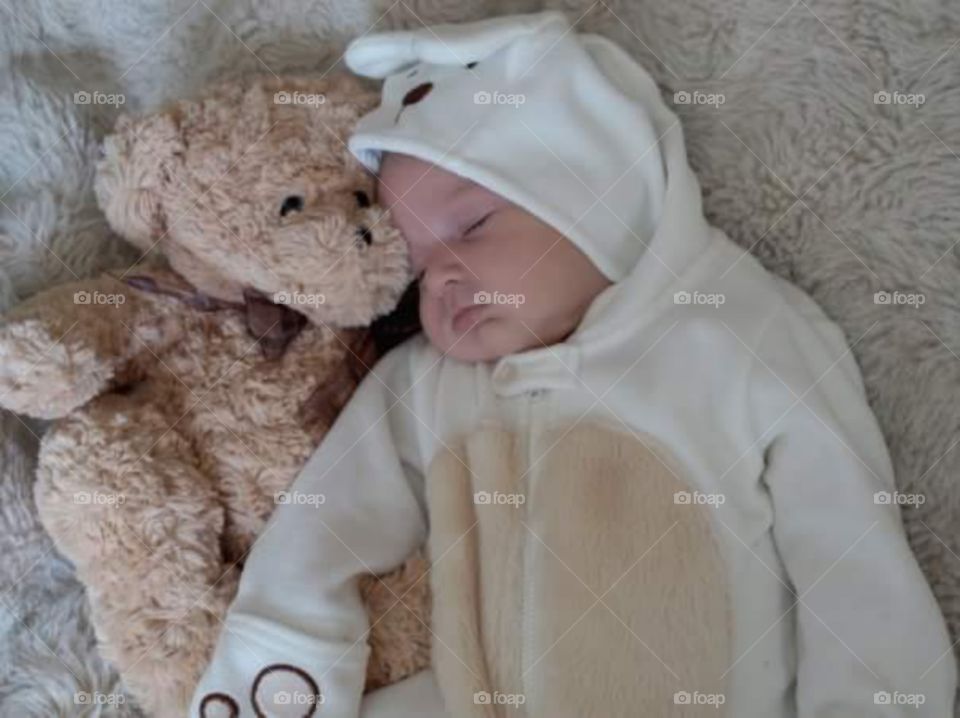 new born chubby baby dressing in a teddy bear suit with her teddy.  sleeping peacefully.