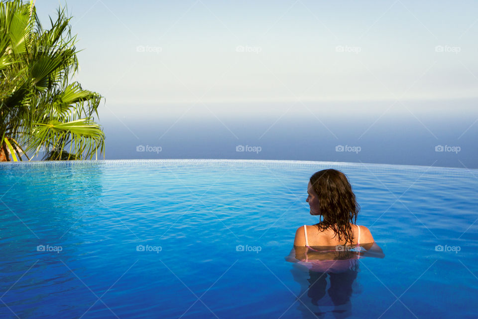 Young girl behind in the pool on the background of the sea. Sunny summer day in Spain.