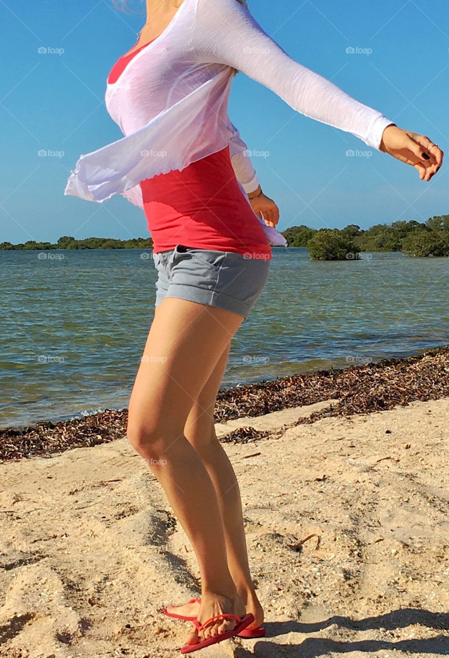 Woman in Red tank top singlet, on windy beach, from the neck down: chest, torso, legs, feet