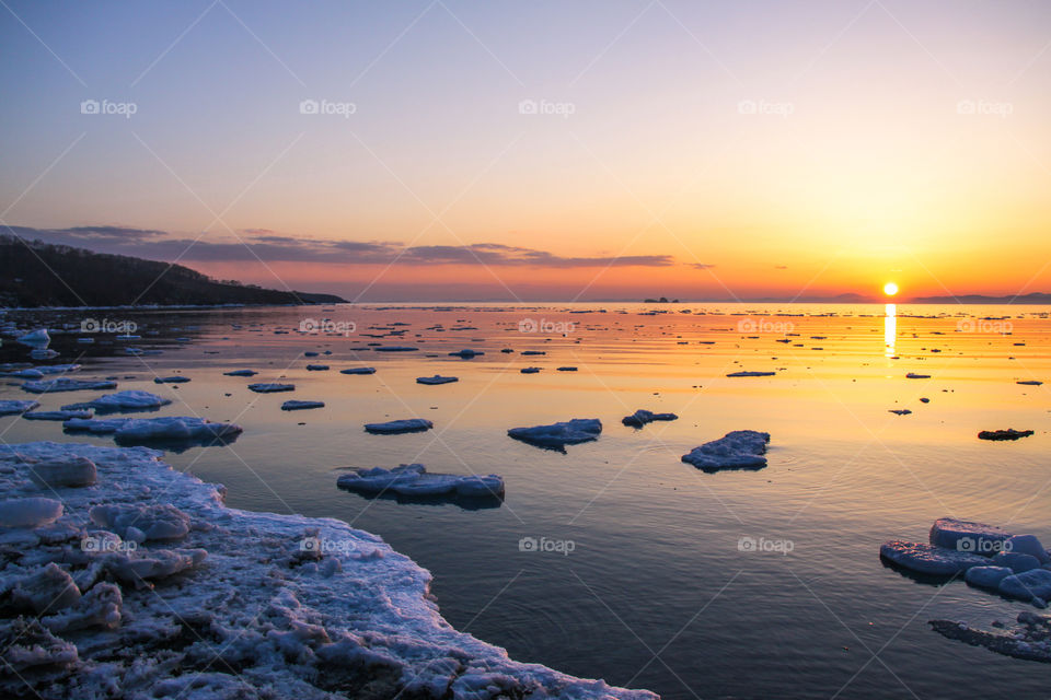Spring sunset on the coast of the sea in a bay with floating ice.