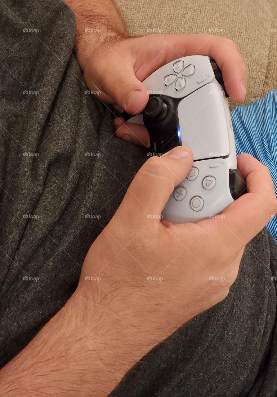 close up of a middle aged man's hands using a Playstation controller to play a video game