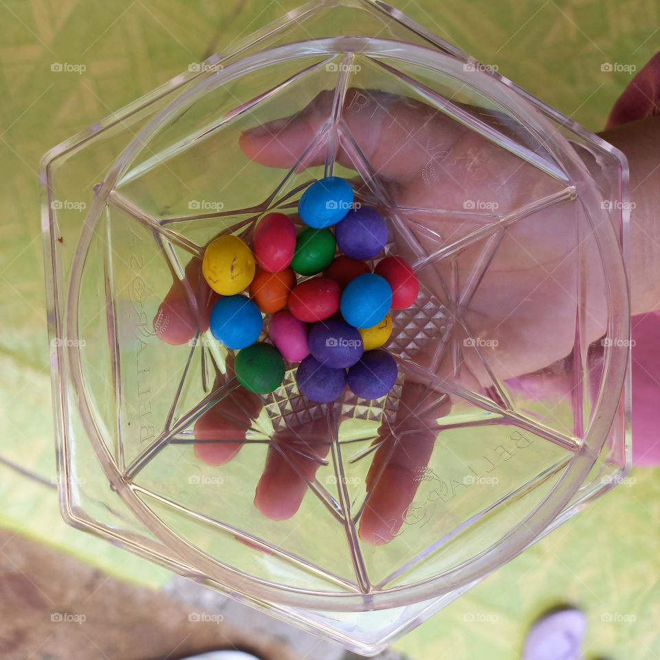 Colorful candies in plastic bowl on palm