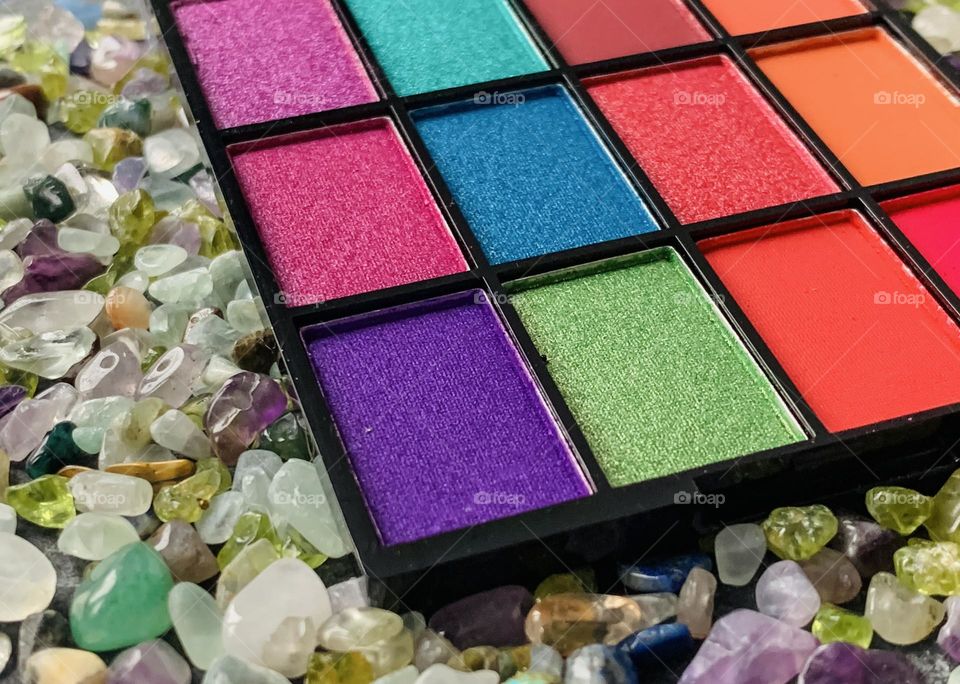 Make up palette in vibrant colours on a bed of assorted, tiny precious stones