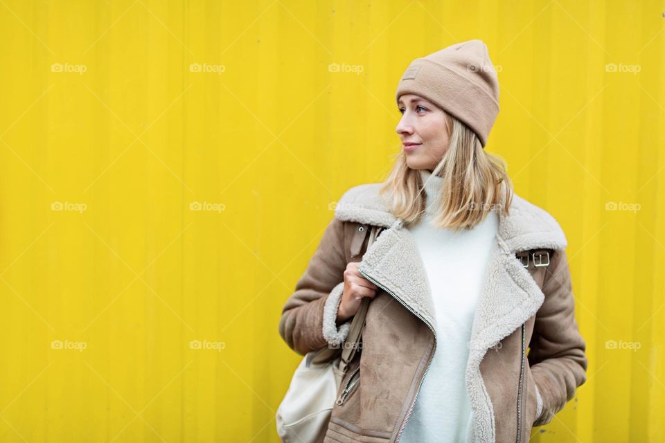 Stylish woman standing near yellow wall 