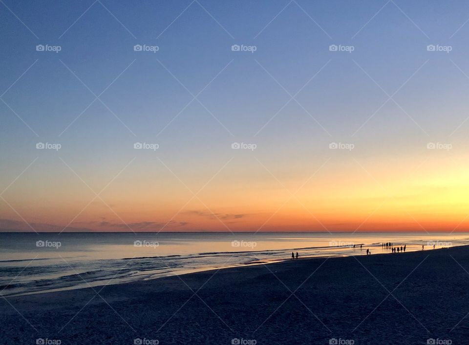 People standing in the shallows on the beach at sunset