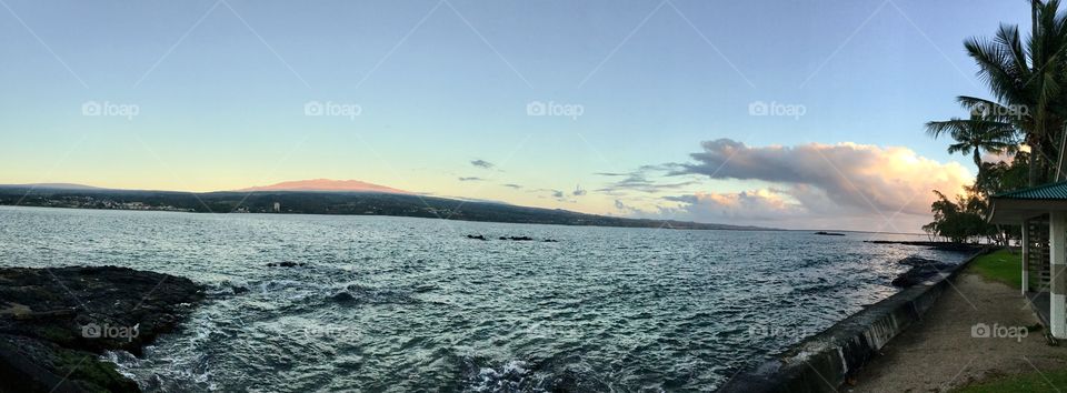 Panorama of sunrise at Hilo Bay with the sun illuminating the volcano