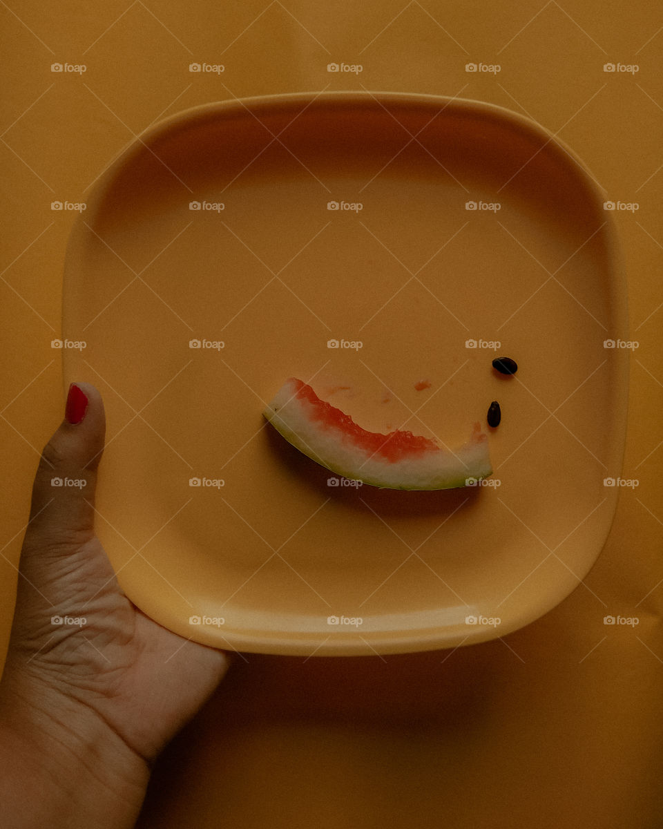 A minimalistic flatlay with a yellow background and yellow plate with some residue of a slice of watermelon.