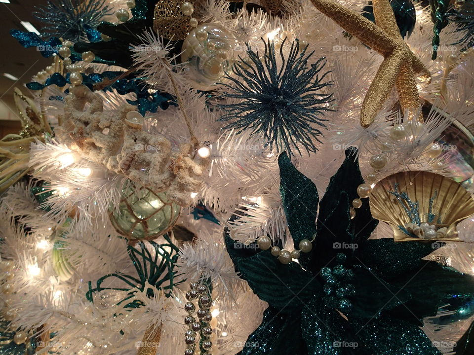 A white Christmas tree decorated with sparkling blue flowers and gold sea shells. 
