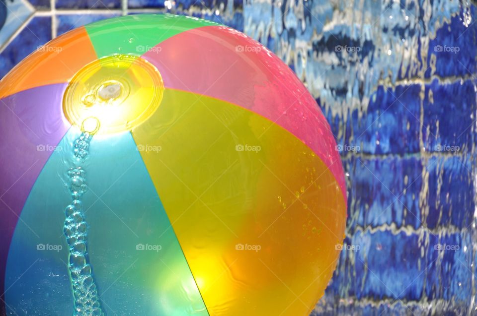 Colorful beach ball floating in a swimming pool with bubbles.