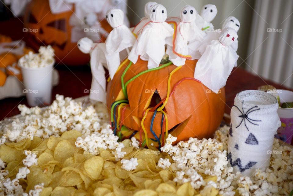 Decoration for Halloween.  The large pumpkin is decorated with napkin ghosts, worm candy chips and popcorn.
