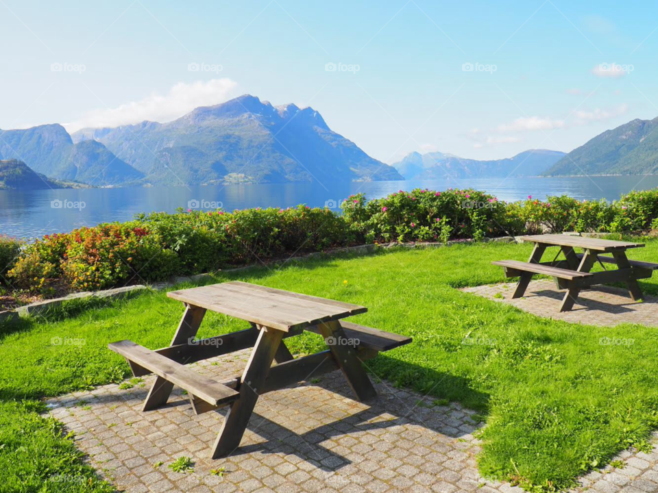 Wood picnic tables in front of flowers, fjord and mountain landscape in Norway