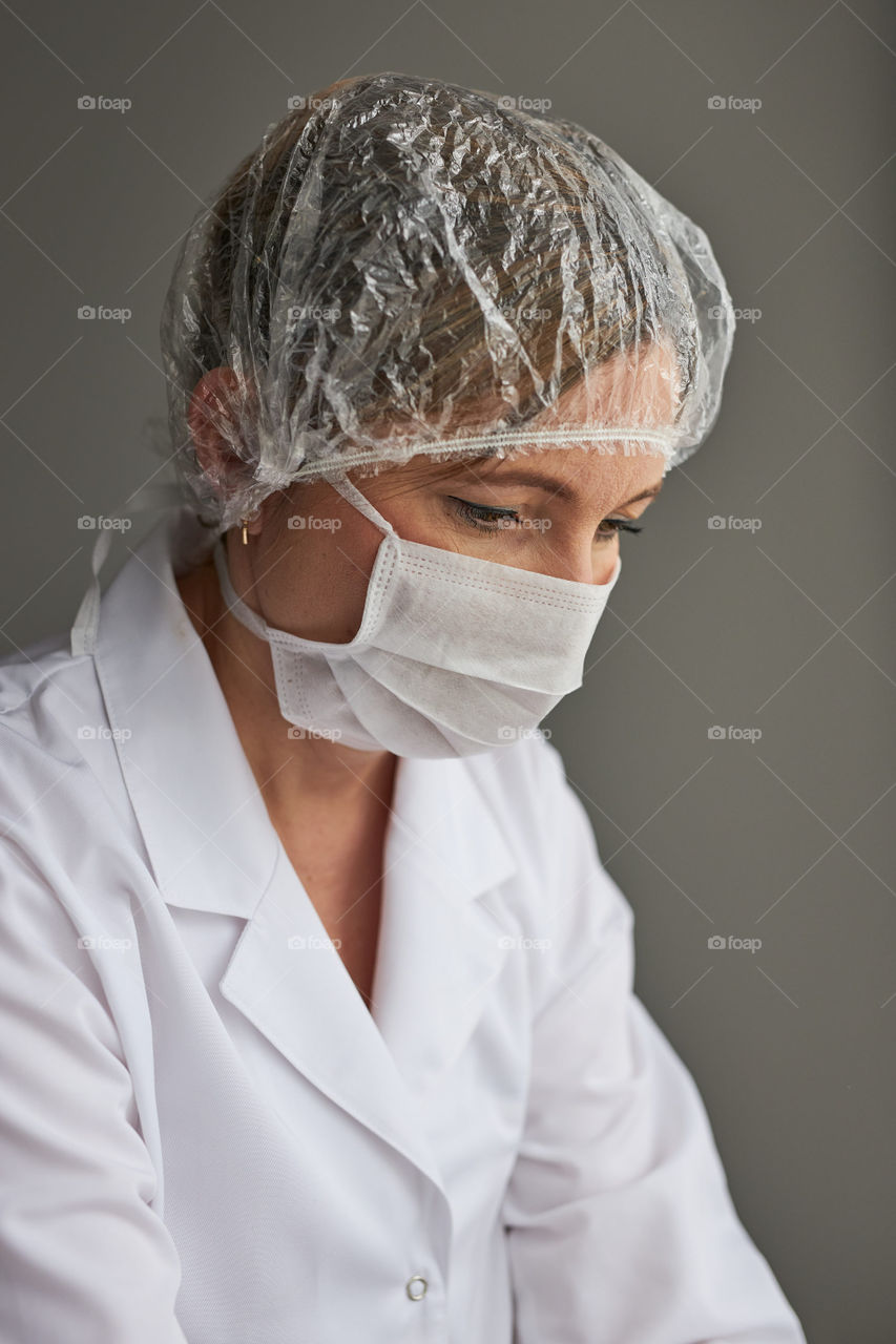 Doctor with face covered with mask. Portrait of young woman wearing the uniform, cap and mask to avoid virus infection and to prevent the spread of disease. Real people, authentic situations