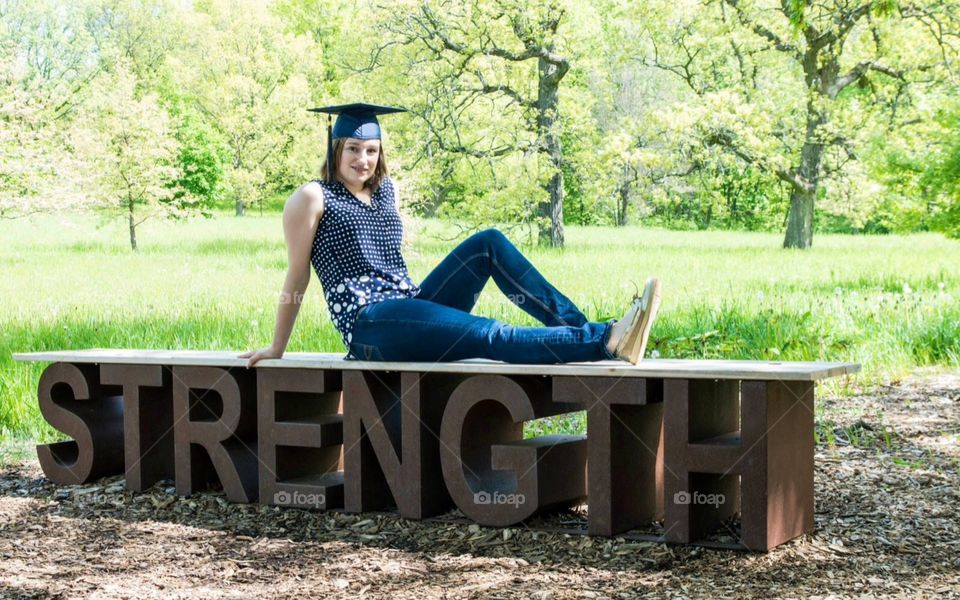 Strength . High school graduation , portrait of a teenage girl , wearing her graduation cap at a forest preserve .