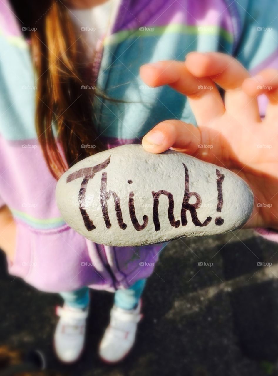 Think! Painted in black ink on a rock held by a girl in the background. You can't see her face. 