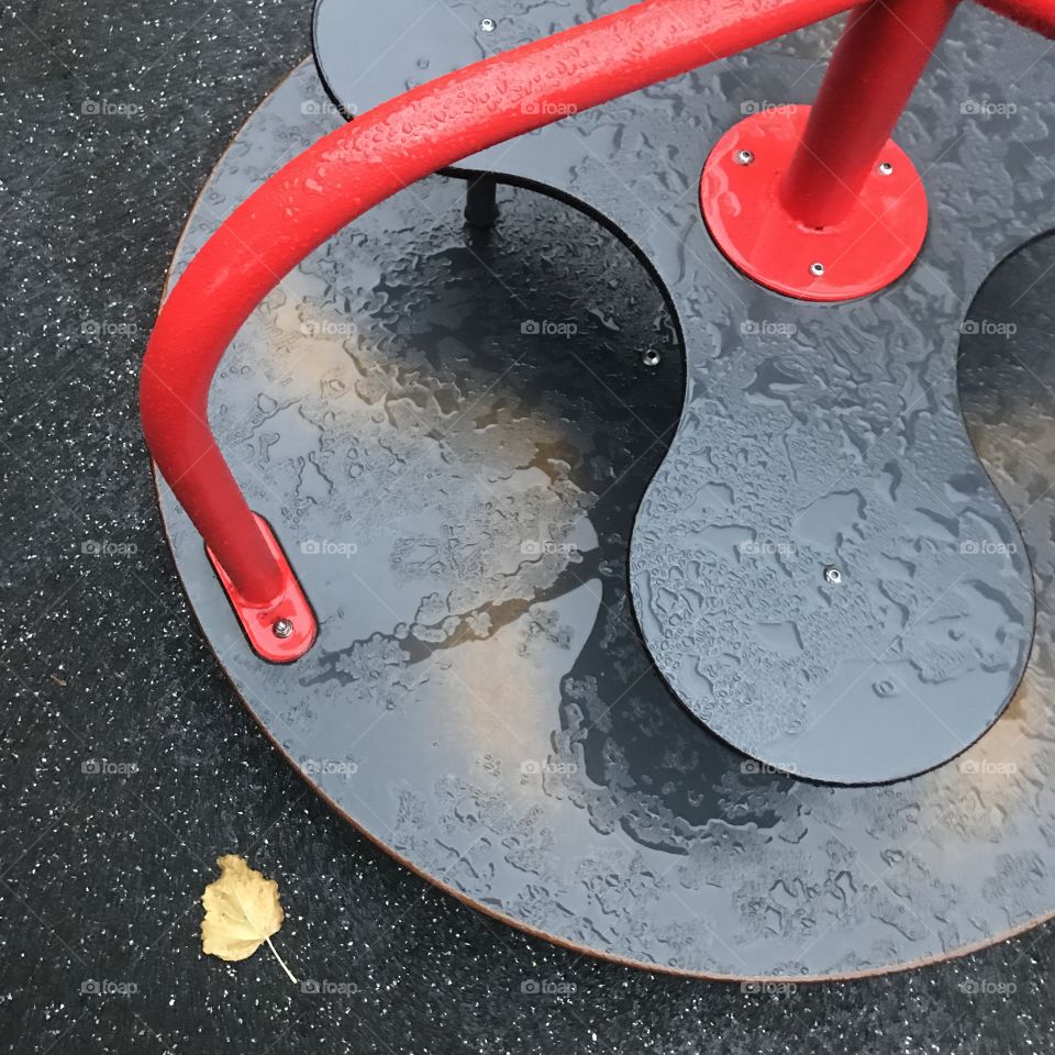 High angle view: Red and black children's carousel wet from rain in the public playground.