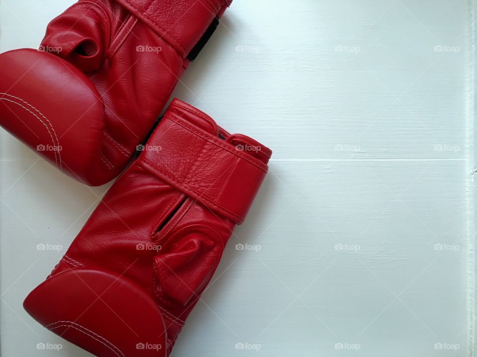 pair of red gloves for boxing exercise on a white wooden background, top view