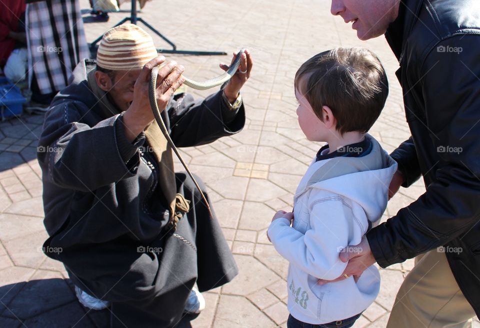 A snake charmer places one of his snakes around a boy's neck