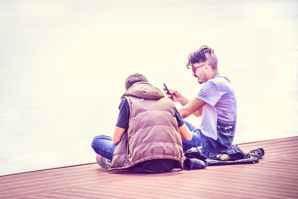 Young People Teenagers Sitiing On The Dock And Checking Mobile Phones
