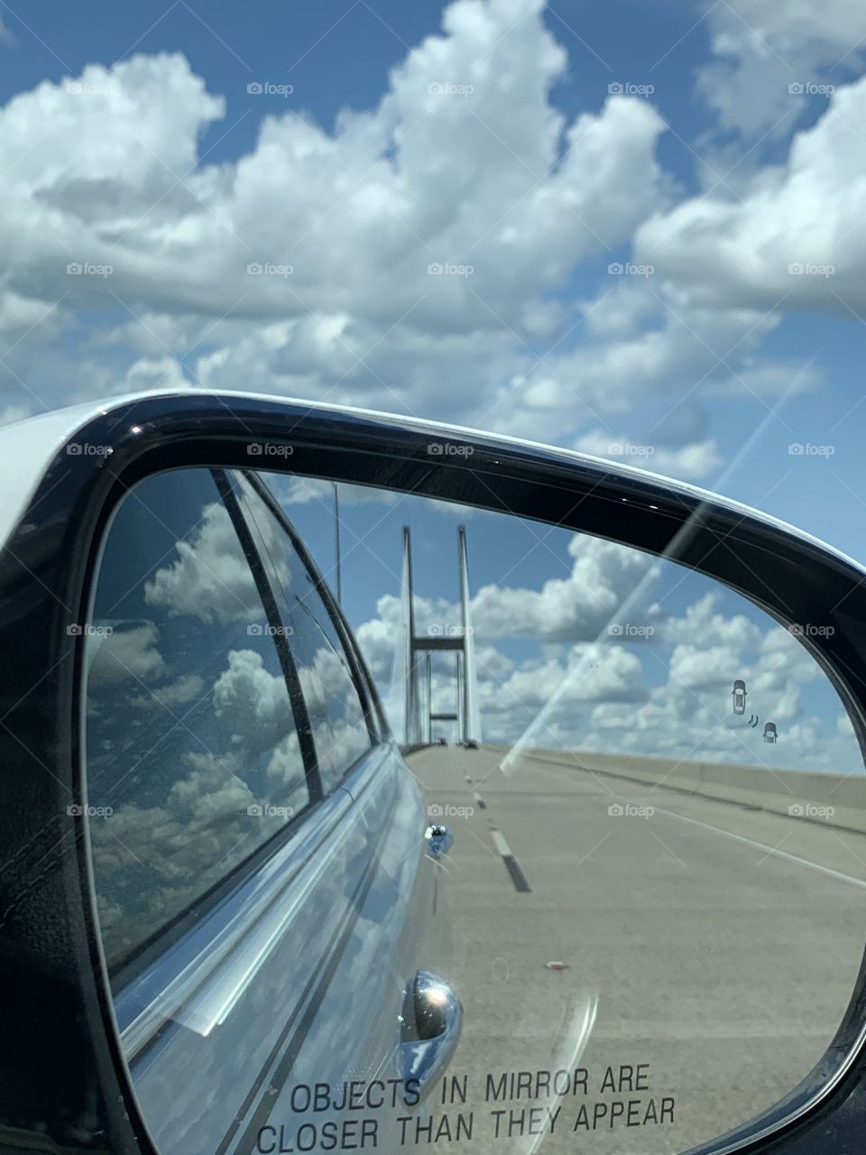 Crossing the bridge with a cloud covered sky through the window and car mirror. Framing the photo draws focus to the subject in the photo by blocking other parts of the image with something in the scene