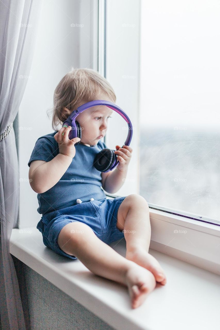 baby sits by the window and listens to music on headphones
