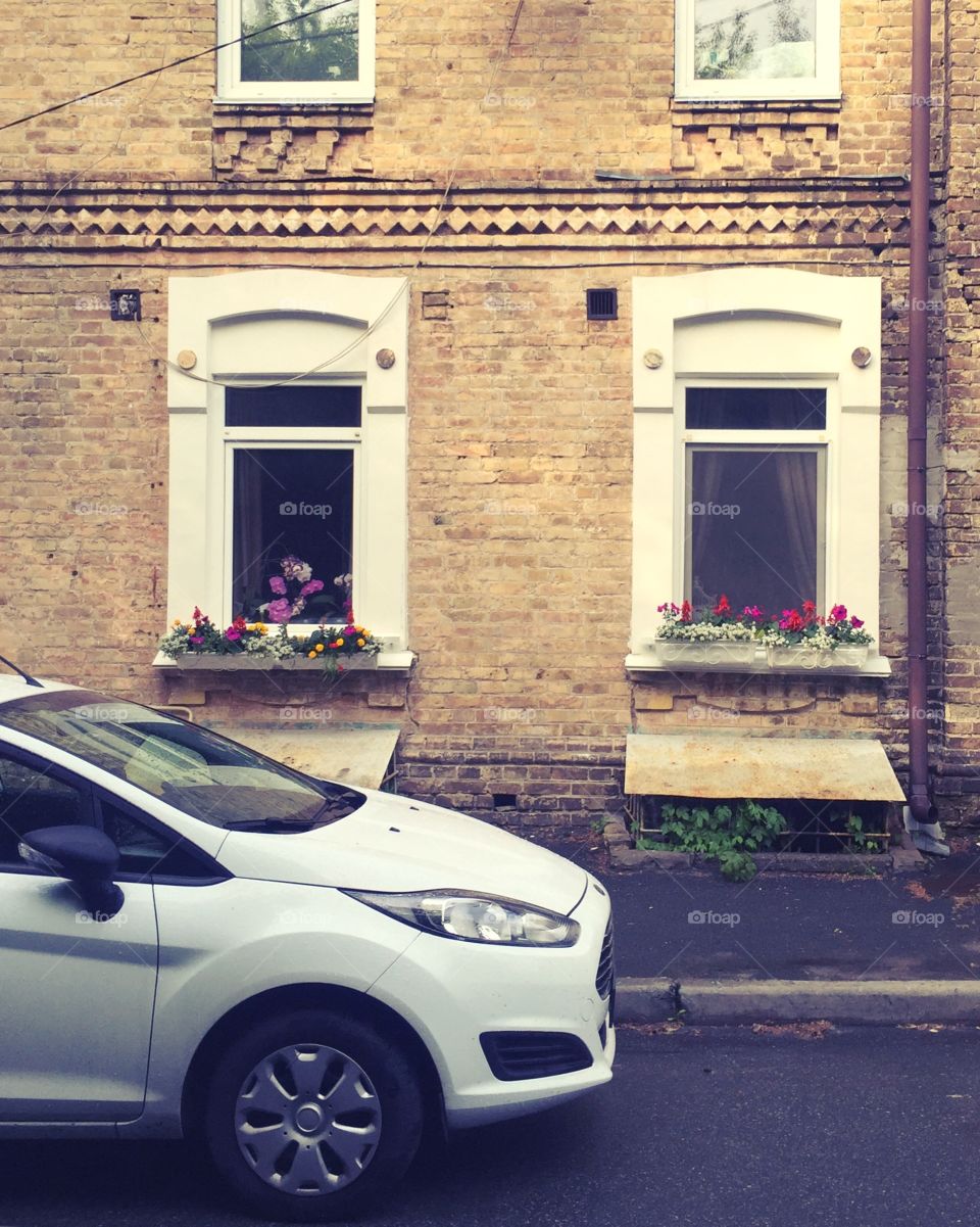 A car parked on the sidewalk near a house with flowers 