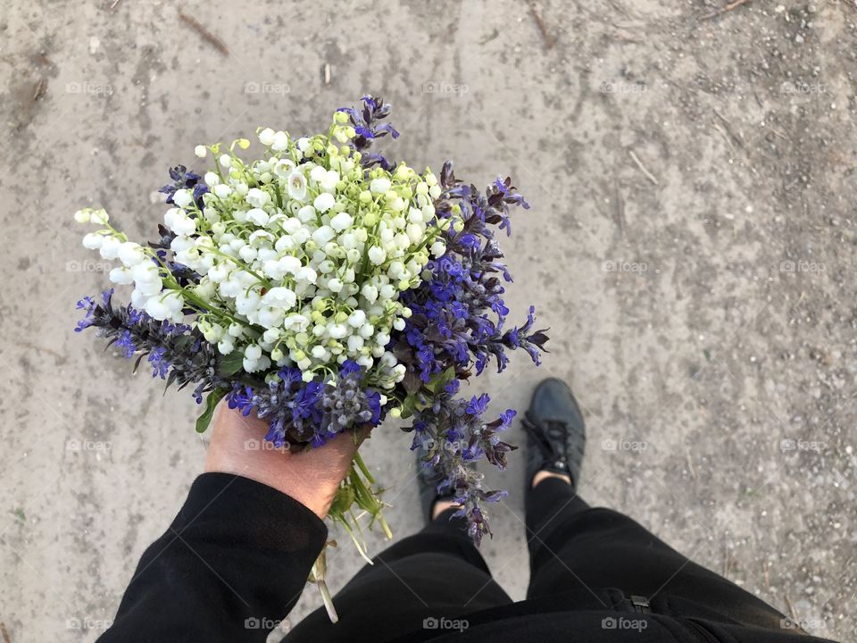 Woman’s hand holding a lily of the valley bouquet with blue flowers